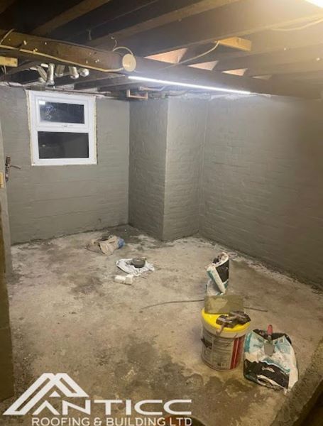 Basement with unfinished concrete floor, exposed beams, window, and painting supplies on the ground.