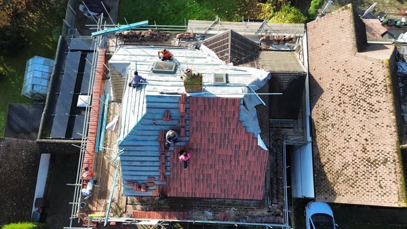 Aerial view of roofers repairing a house roof with blue tarps and red shingles.