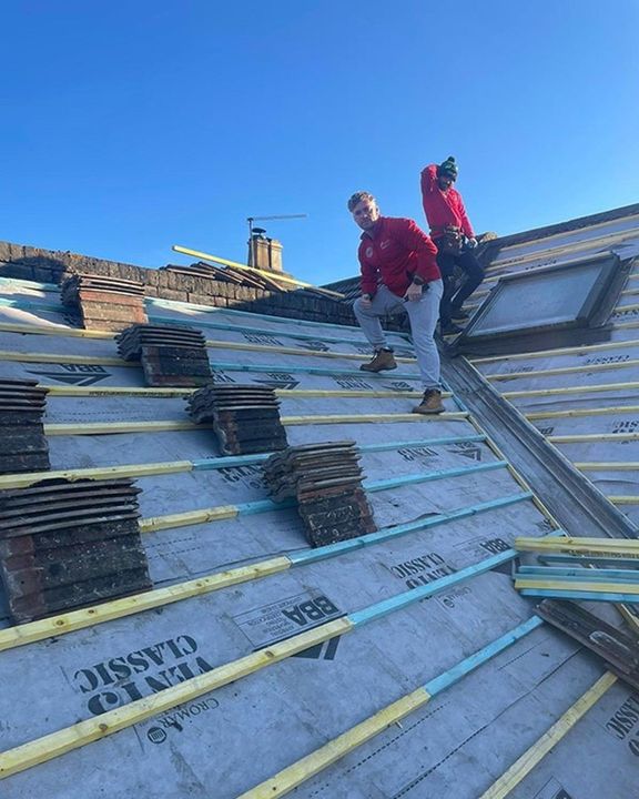 Two workers on a steep roof installing panels under a clear blue sky