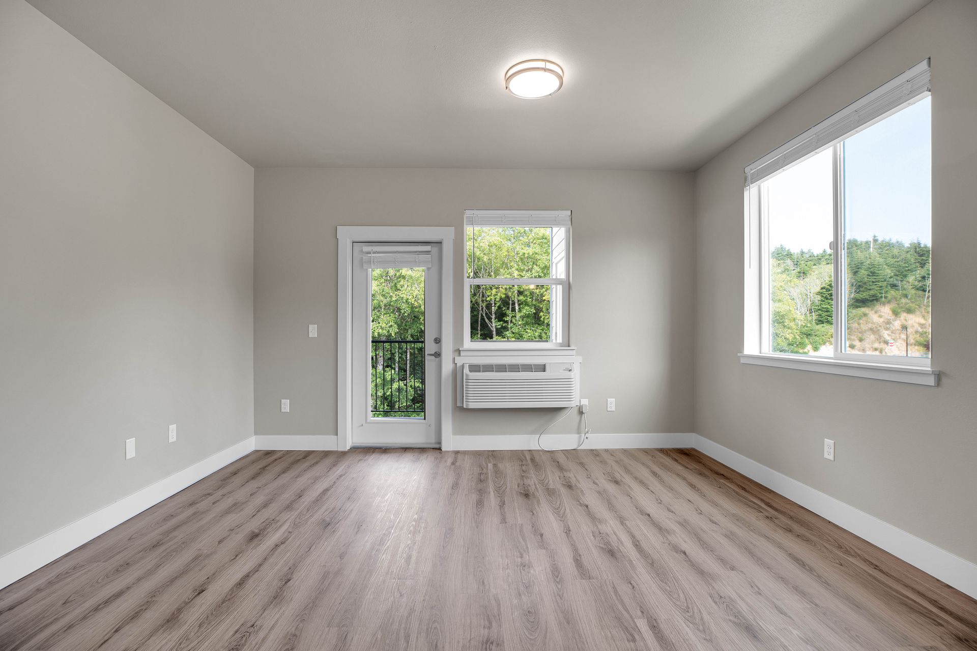 An empty living room with hardwood floors and a balcony.