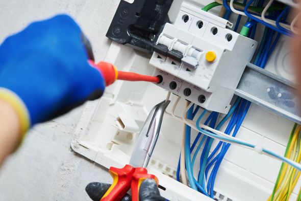 Elettricista che testa un quadro elettrico con sonde rosse e guanti blu; i fili sono visibili all'interno dell'armadio.