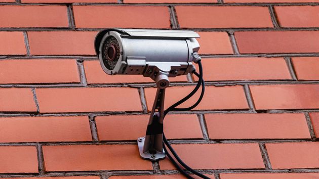 Telecamera di sicurezza argentata montata su un muro di mattoni, inclinata verso il basso.