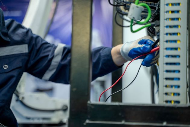Tecnico con guanti blu che cabla un quadro elettrico con fili rossi e neri