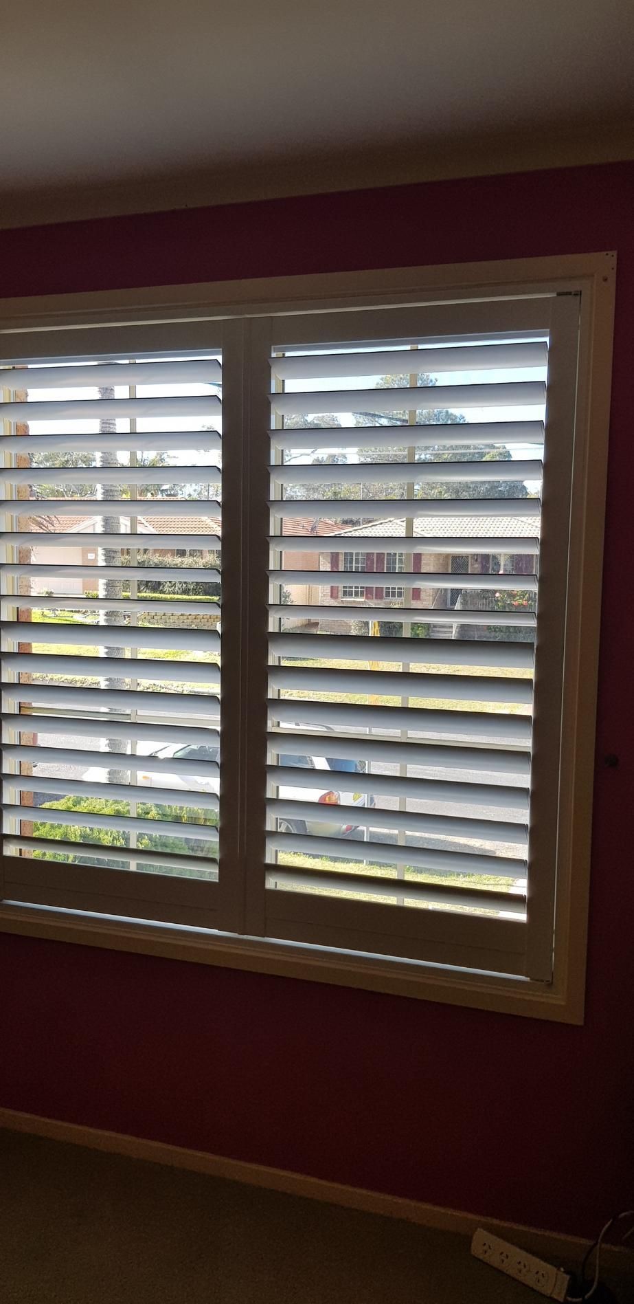 A Bedroom With a Window With Shutters on It and a Pink Wall — Design 2000 Blinds & Awnings In San Remo, NSW