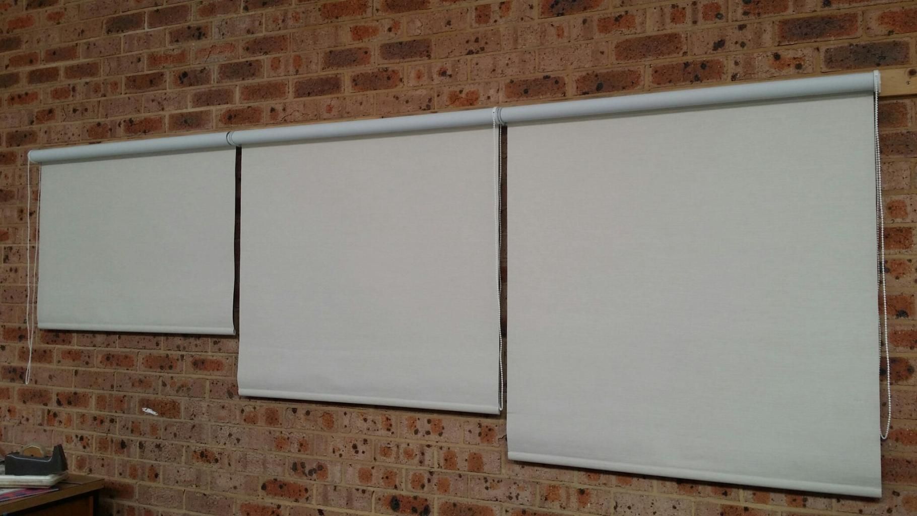 Three White Blinds Are Hanging on a Brick Wall — Design 2000 Blinds & Awnings In San Remo, NSW