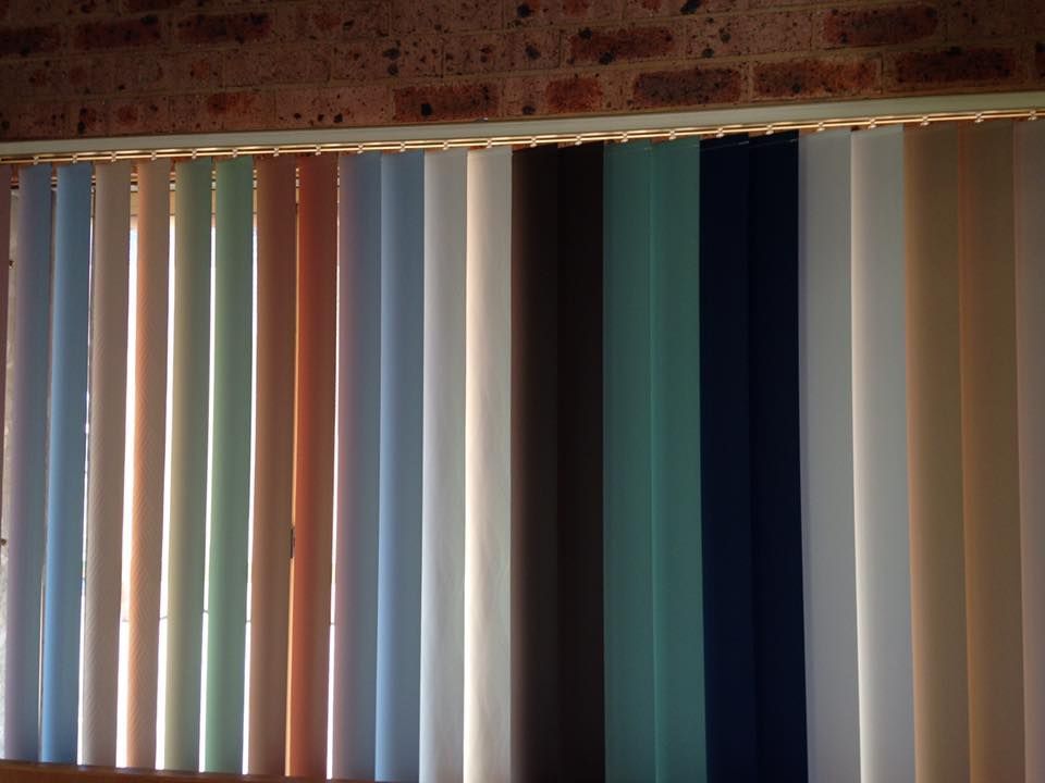 A Row of Vertical Blinds in Different Colors Against a Brick Wall — Design 2000 Blinds & Awnings In San Remo, NSW
