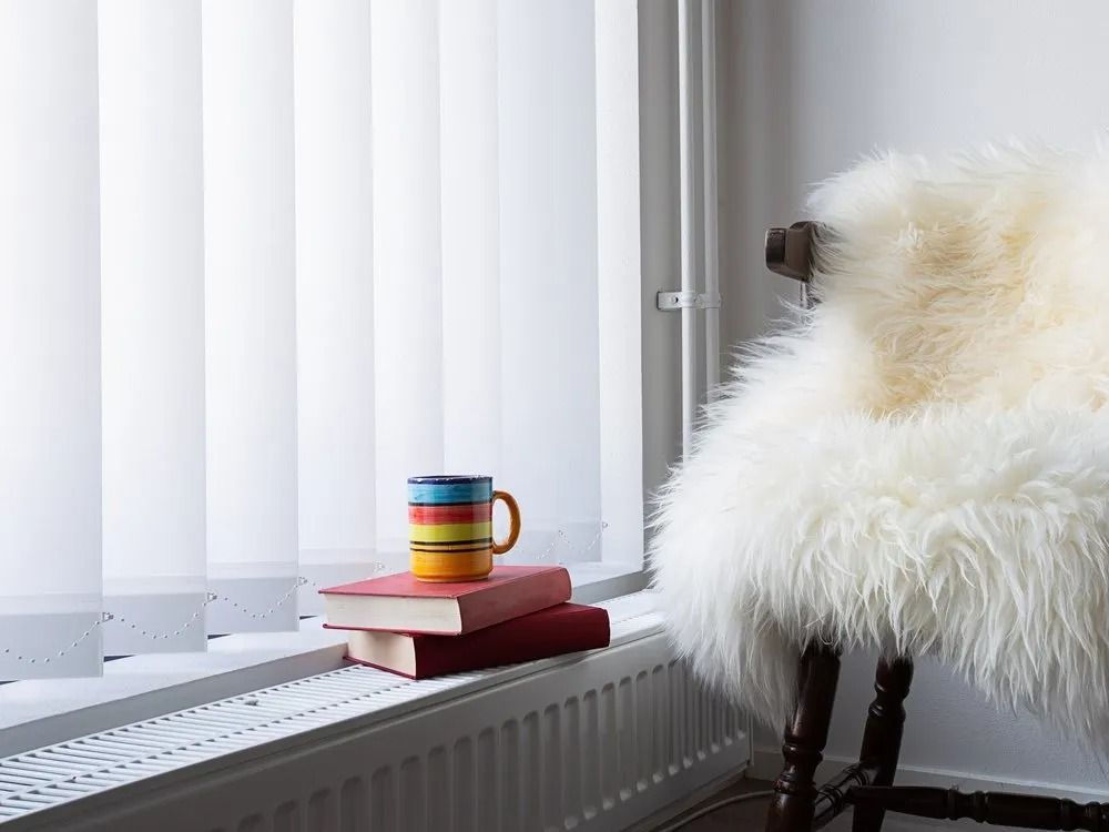 A Chair With a Fur Blanket and a Stack of Books on the Window Sill — Design 2000 Blinds & Awnings In San Remo, NSW