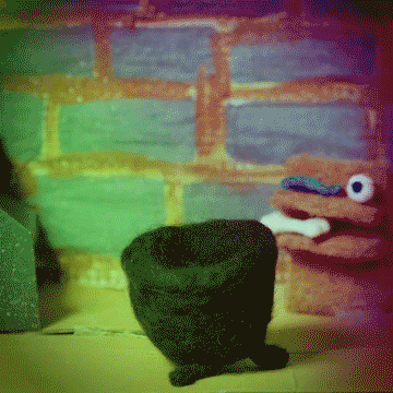 Clay figures in front of a colorful brick wall, with a dark pot and a pink character on the right.