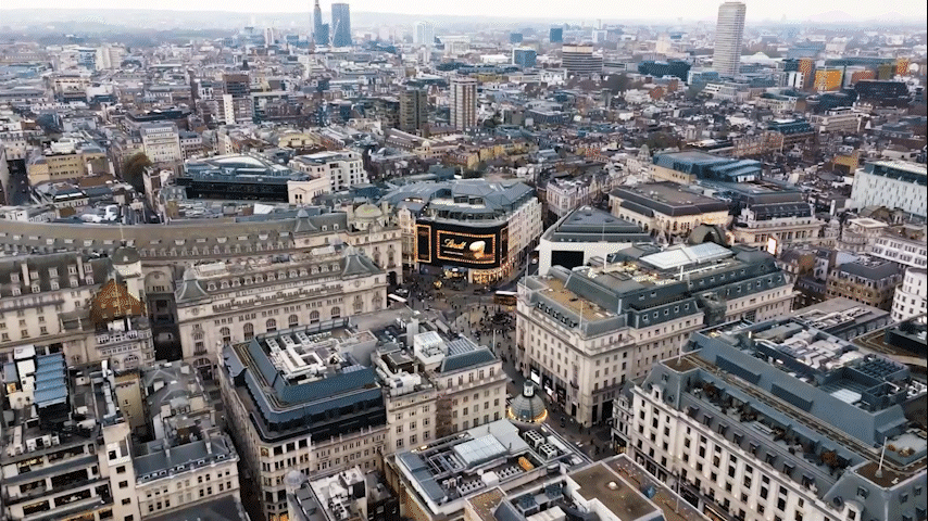 Aerial view of a dense city center with historic buildings and a large plaza under a cloudy sky
