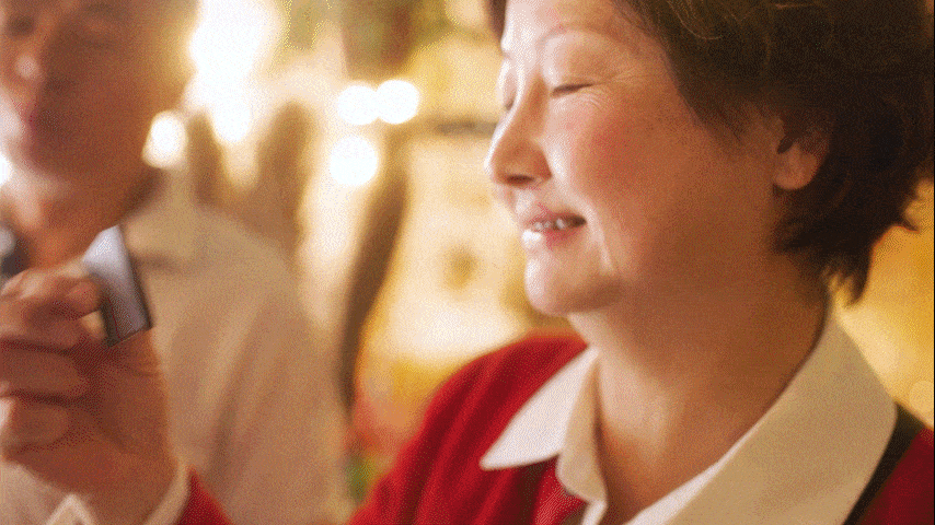Person in a red sweater with eyes closed, holding a small item in a warmly lit indoor setting