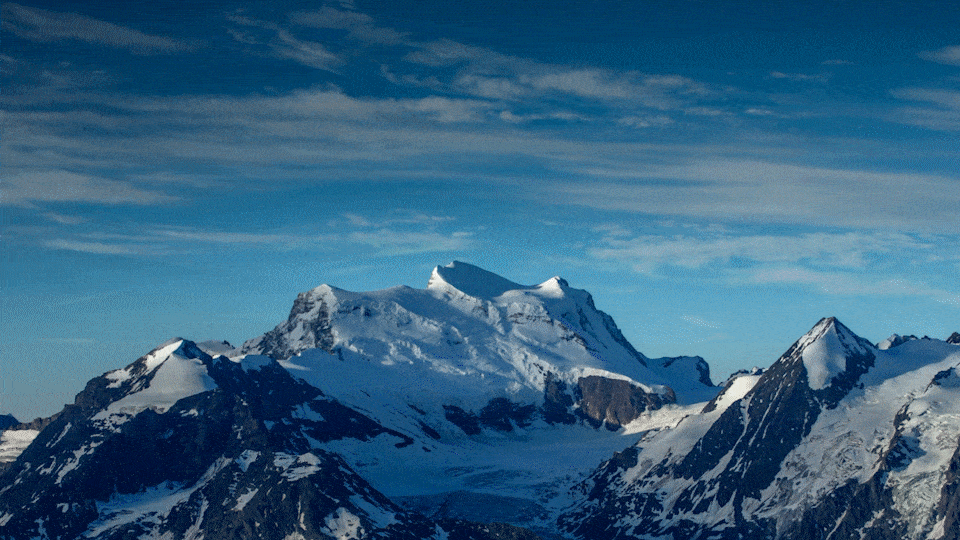 Snow-covered mountain peaks under a blue sky with wispy clouds.