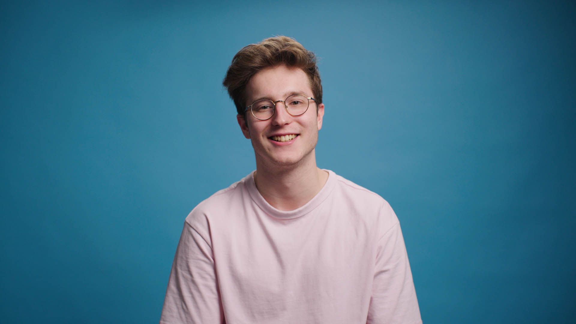 A man in a plaid shirt is smiling in front of a blue background.