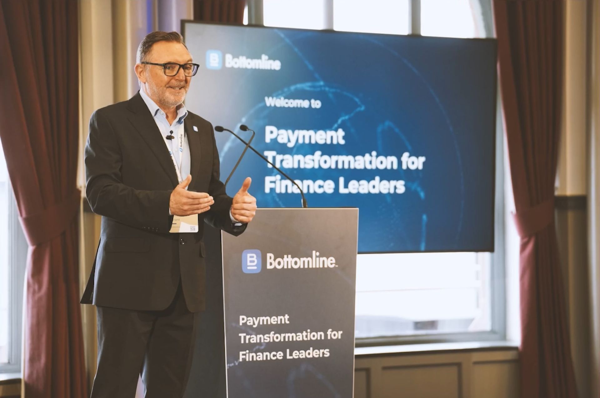 Man in a suit presenting beside a screen reading “Payment Transformation for Finance Leaders”