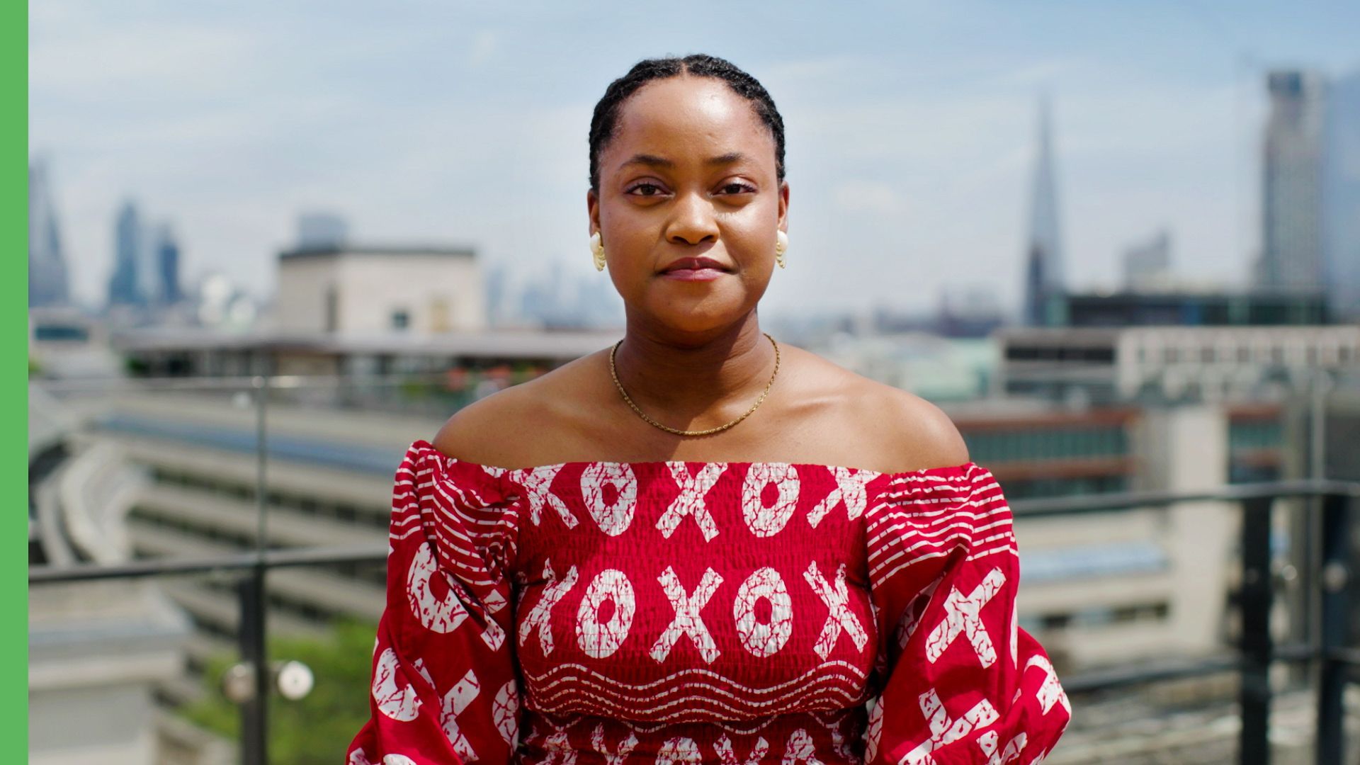 Woman in a red patterned off-shoulder top standing outdoors with city buildings in the background