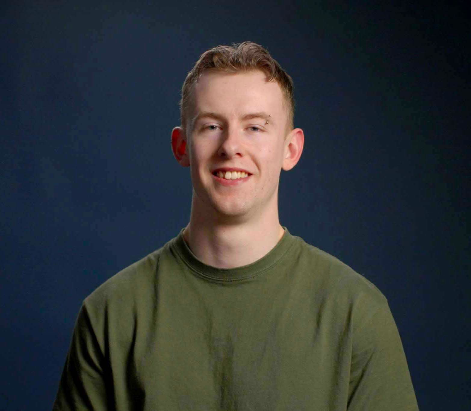 A man in a plaid shirt is smiling in front of a blue background.