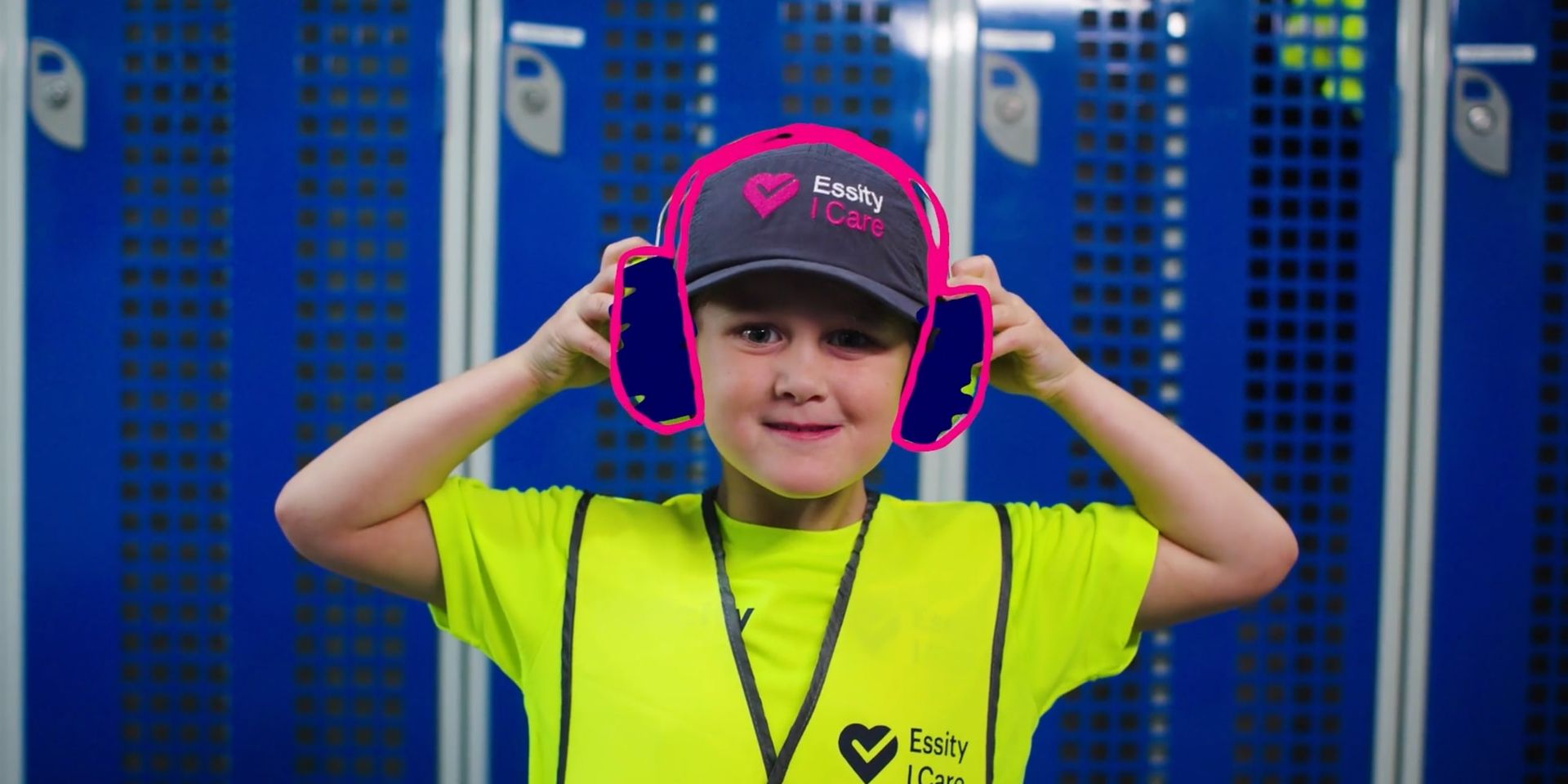 Child in a neon yellow shirt and black cap adjusting bright pink headphones in front of blue lockers