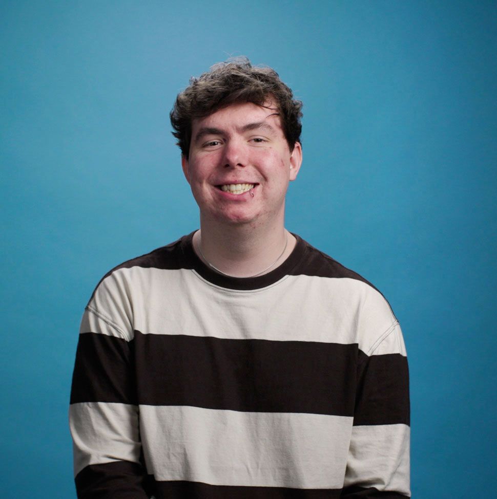 A young man in a black shirt is smiling and looking at the camera.