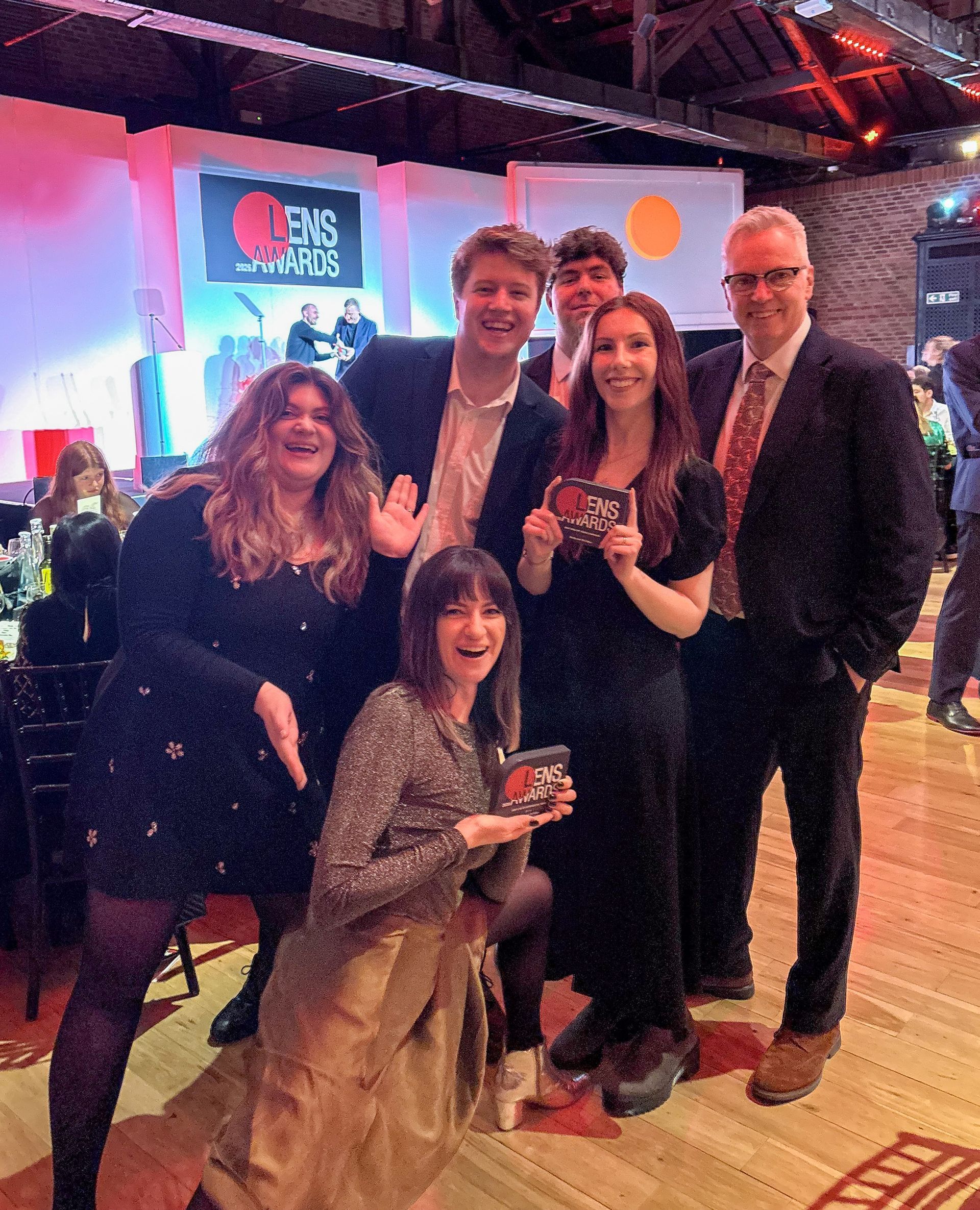 Group posing with awards at a lively indoor event, smiling under colorful lights.
