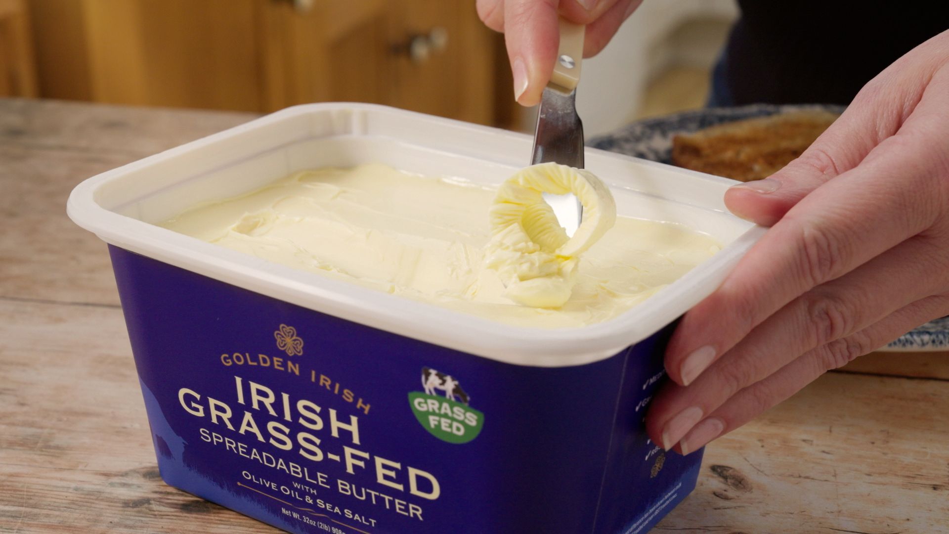 Hands scooping butter from a blue tub labeled Irish grass-fed butter