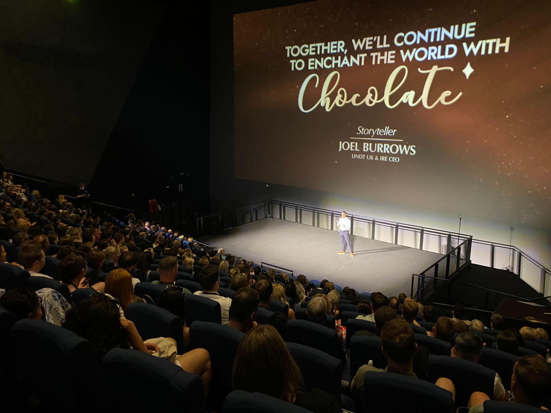 Conference stage with large “Chocolate” presentation screen and audience in theater seating