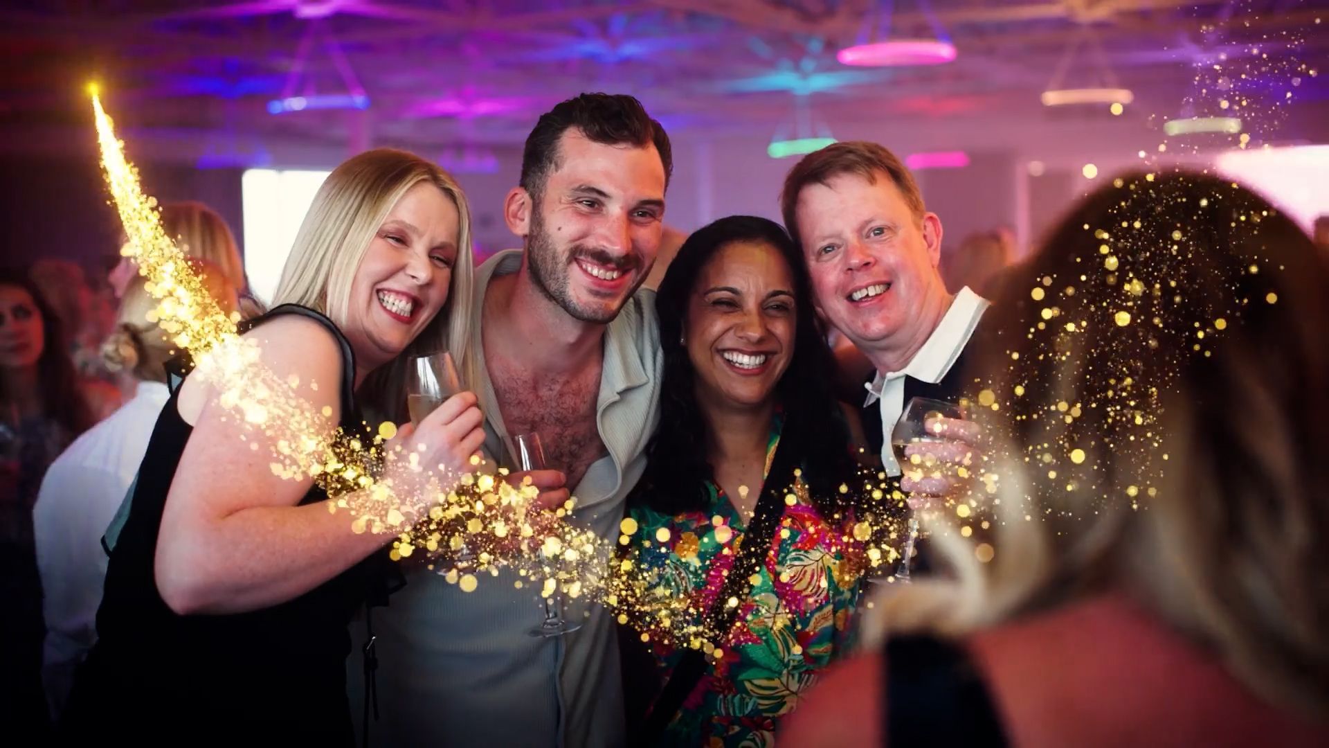 Four friends smiling and posing at a party with sparklers and colorful lights