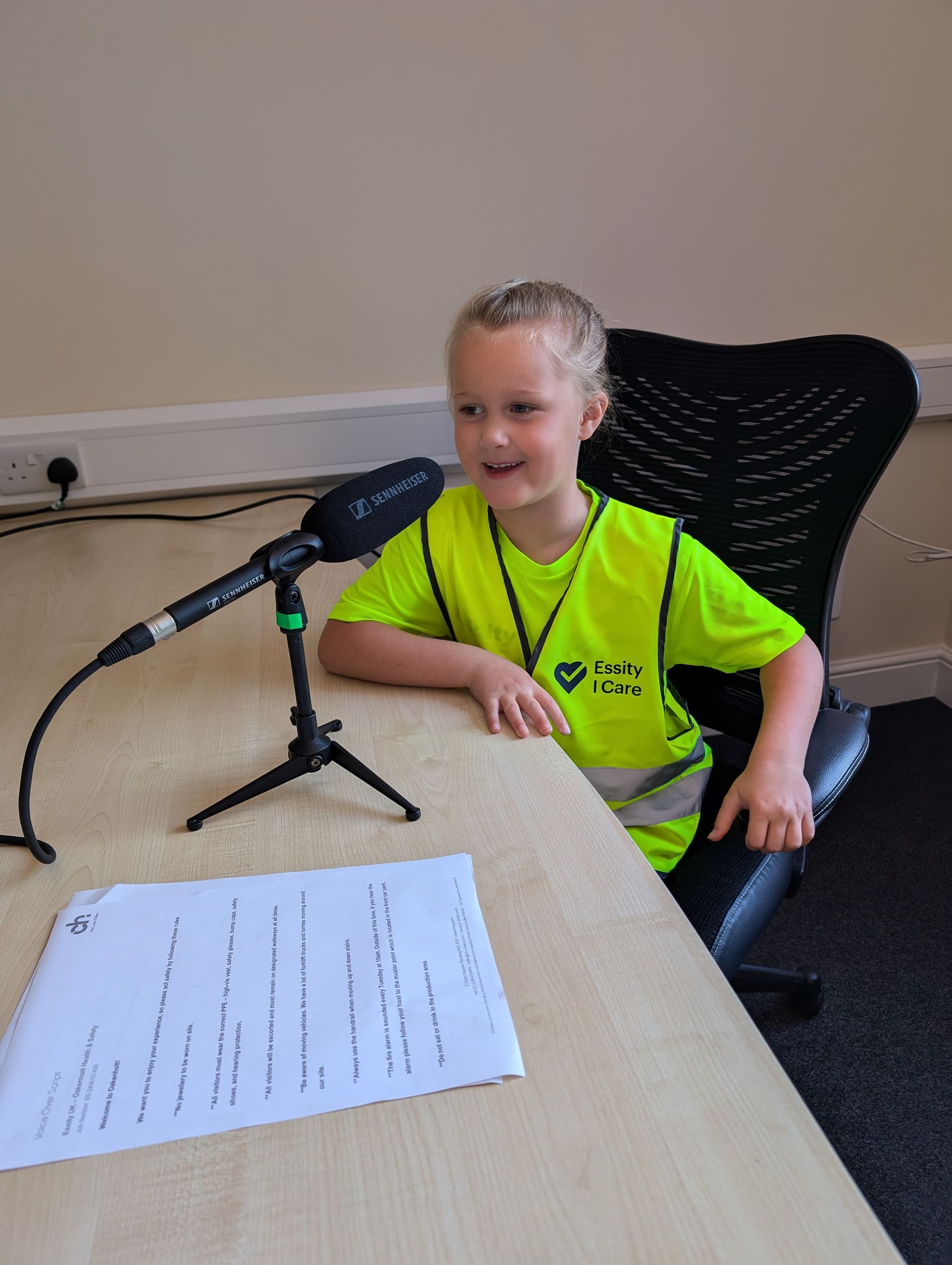 Child speaking into a microphone at a table, with a paper in front, in a classroom setting