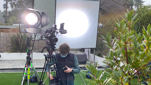 A man is standing in front of a camera on a tripod.