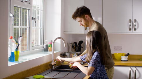 A man and a girl are washing dishes in a kitchen sink.