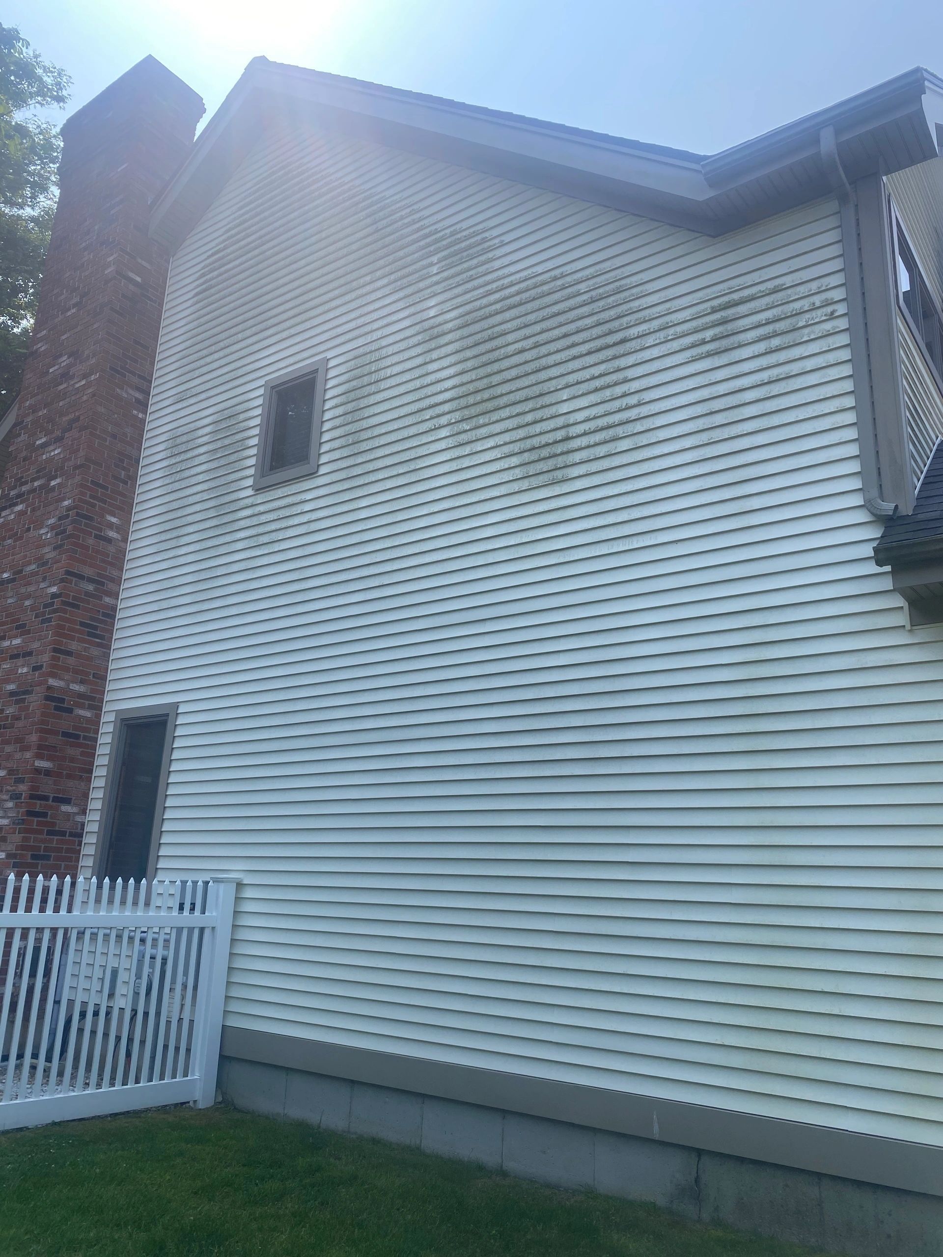White vinyl-sided house exterior with a small window, roofline, and white fence by a grassy yard.