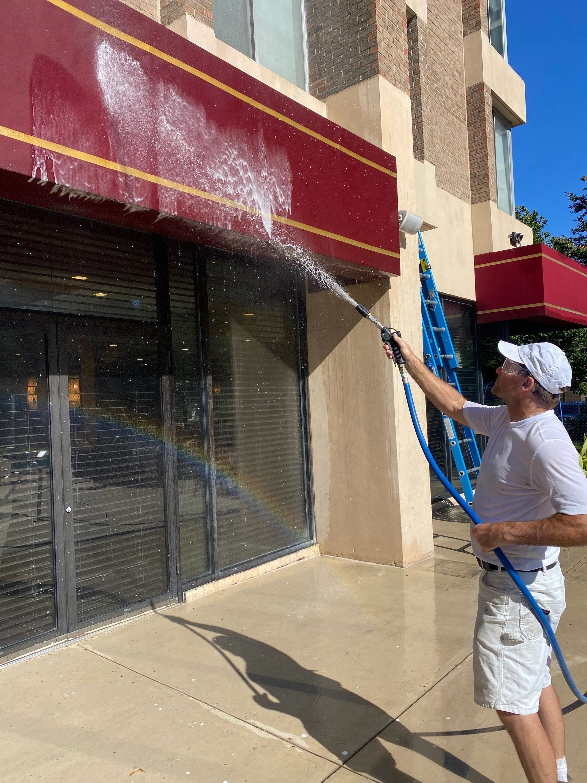Worker spraying water to clean a building storefront with a hose outdoors