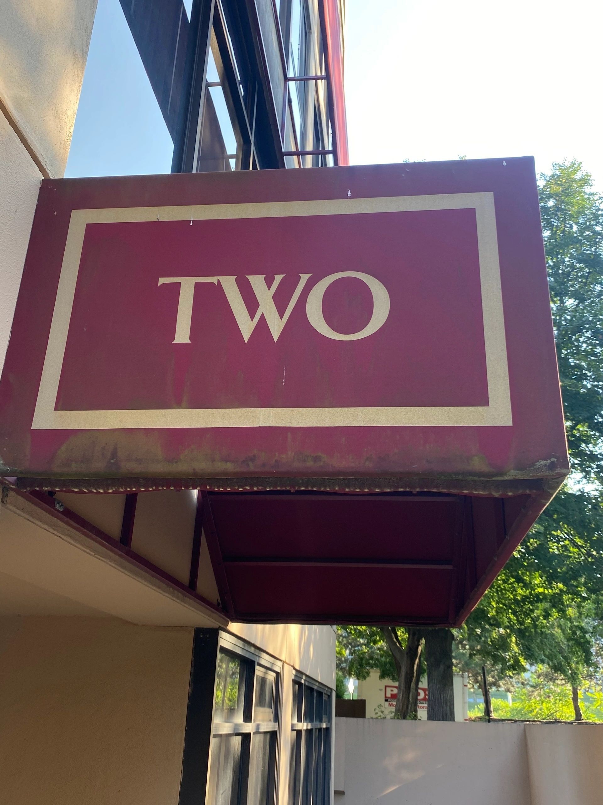 Maroon storefront sign with the word “TWO” above a sidewalk awning