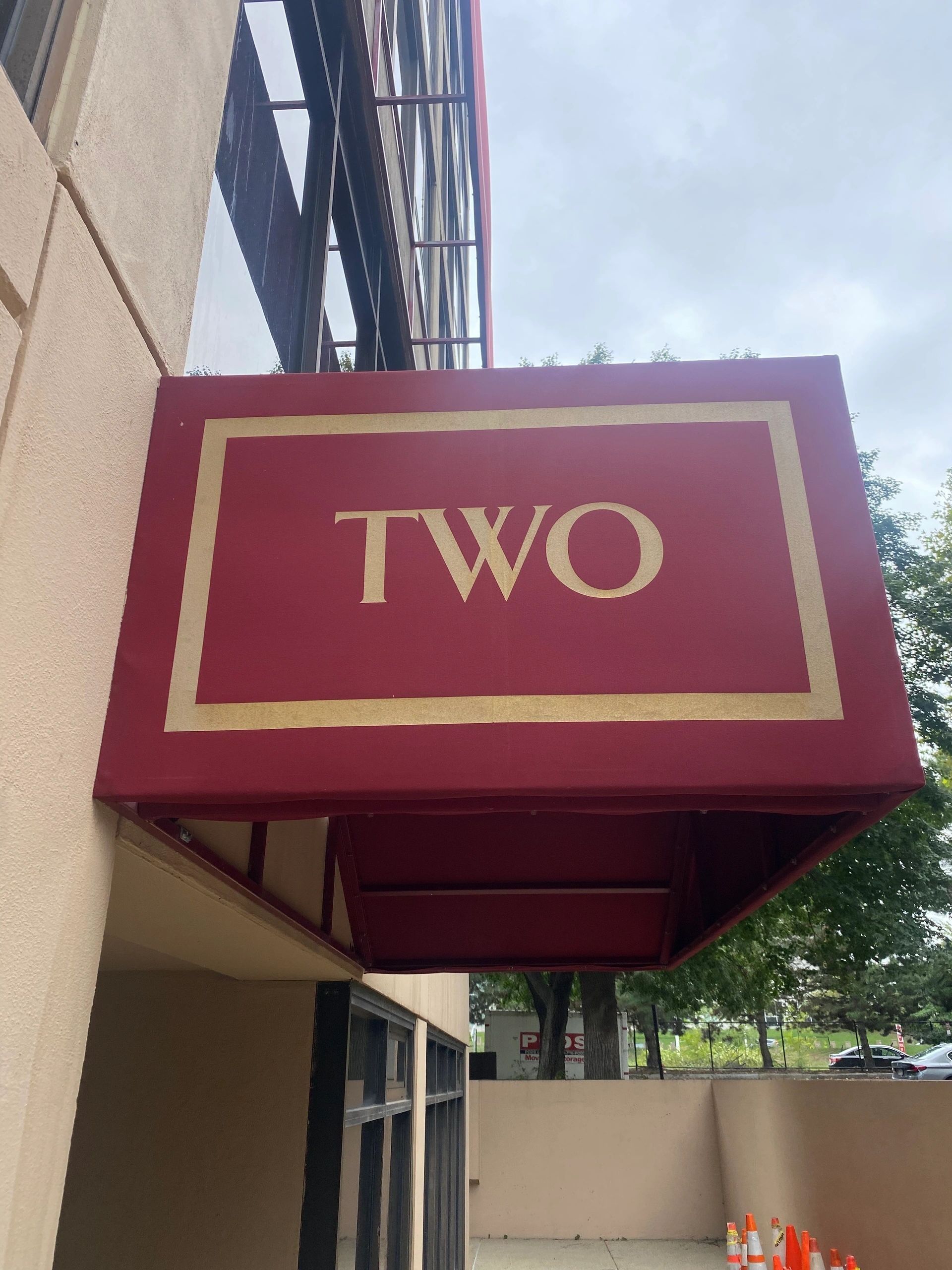 Red awning sign with gold border and the word “TWO” on a building exterior.