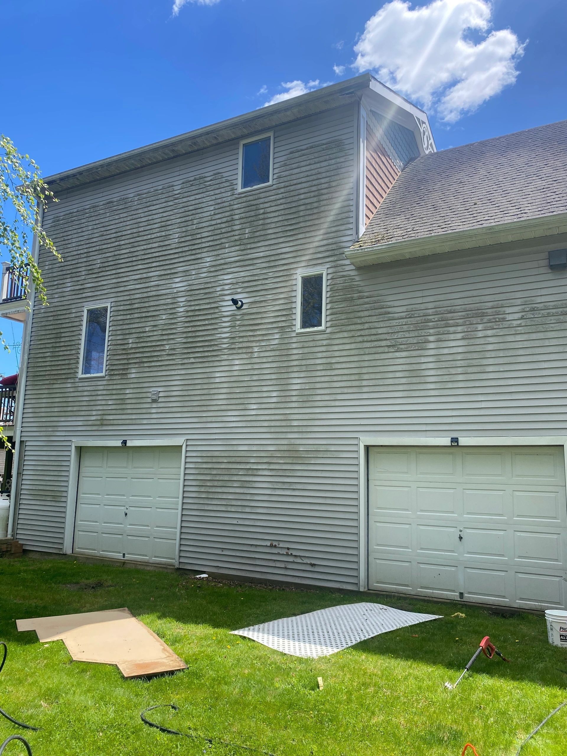 Exterior of a gray house with wavy siding, two garage doors, and a grassy yard under a blue sky