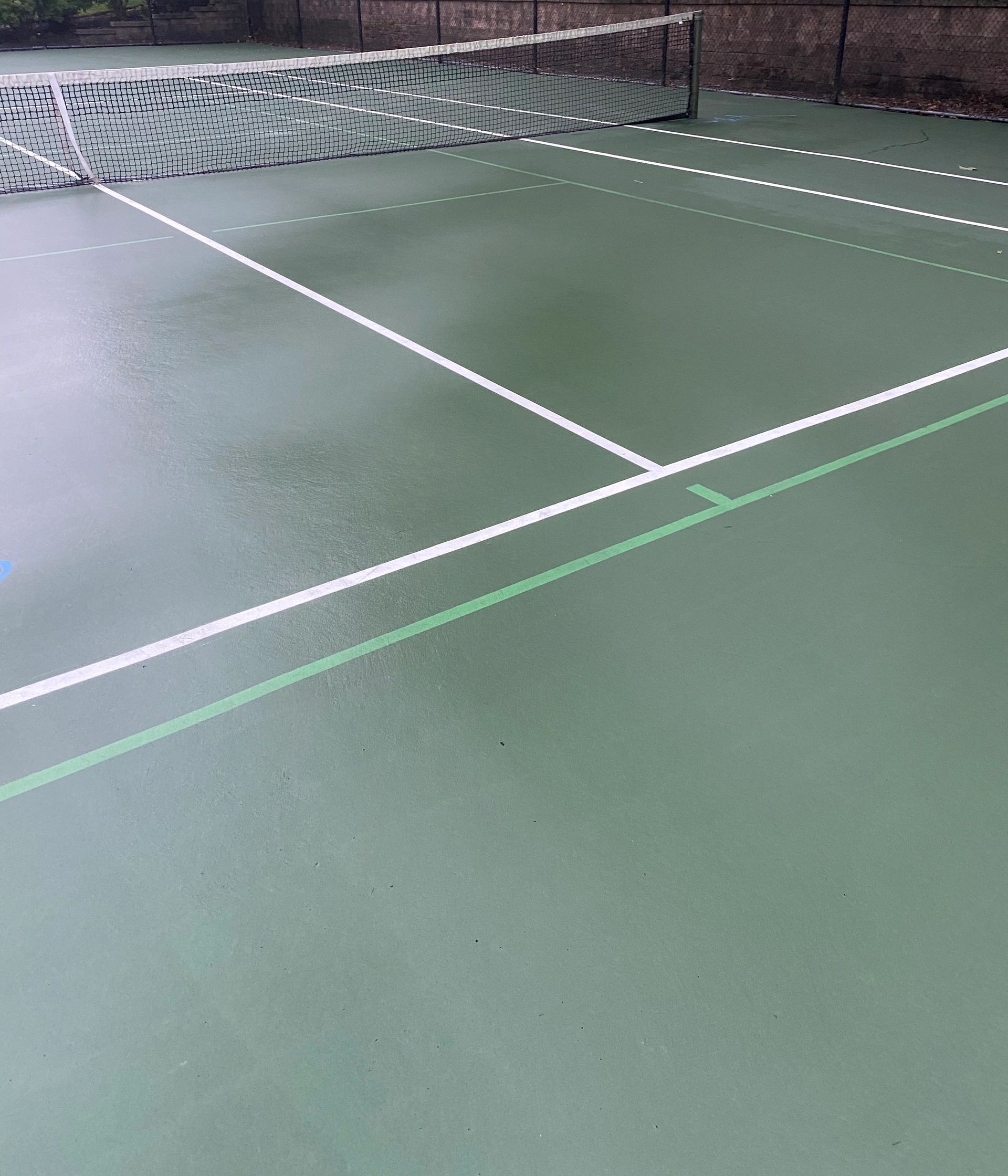 Outdoor tennis court with white lines and a net on a green surface