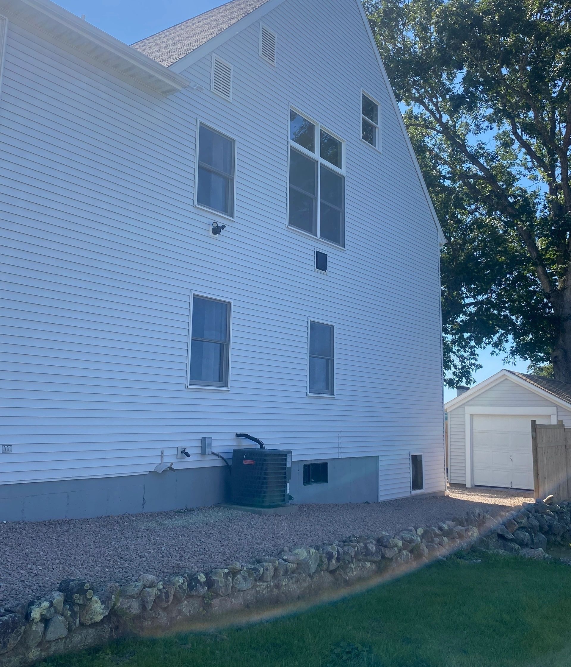 White house exterior with wavy siding, windows, stone border, and a detached garage beside a lawn.
