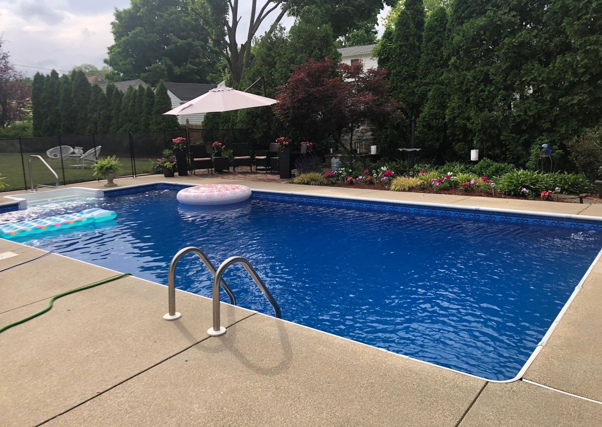 Backyard pool with blue water, concrete deck, and white patio umbrella surrounded by trees