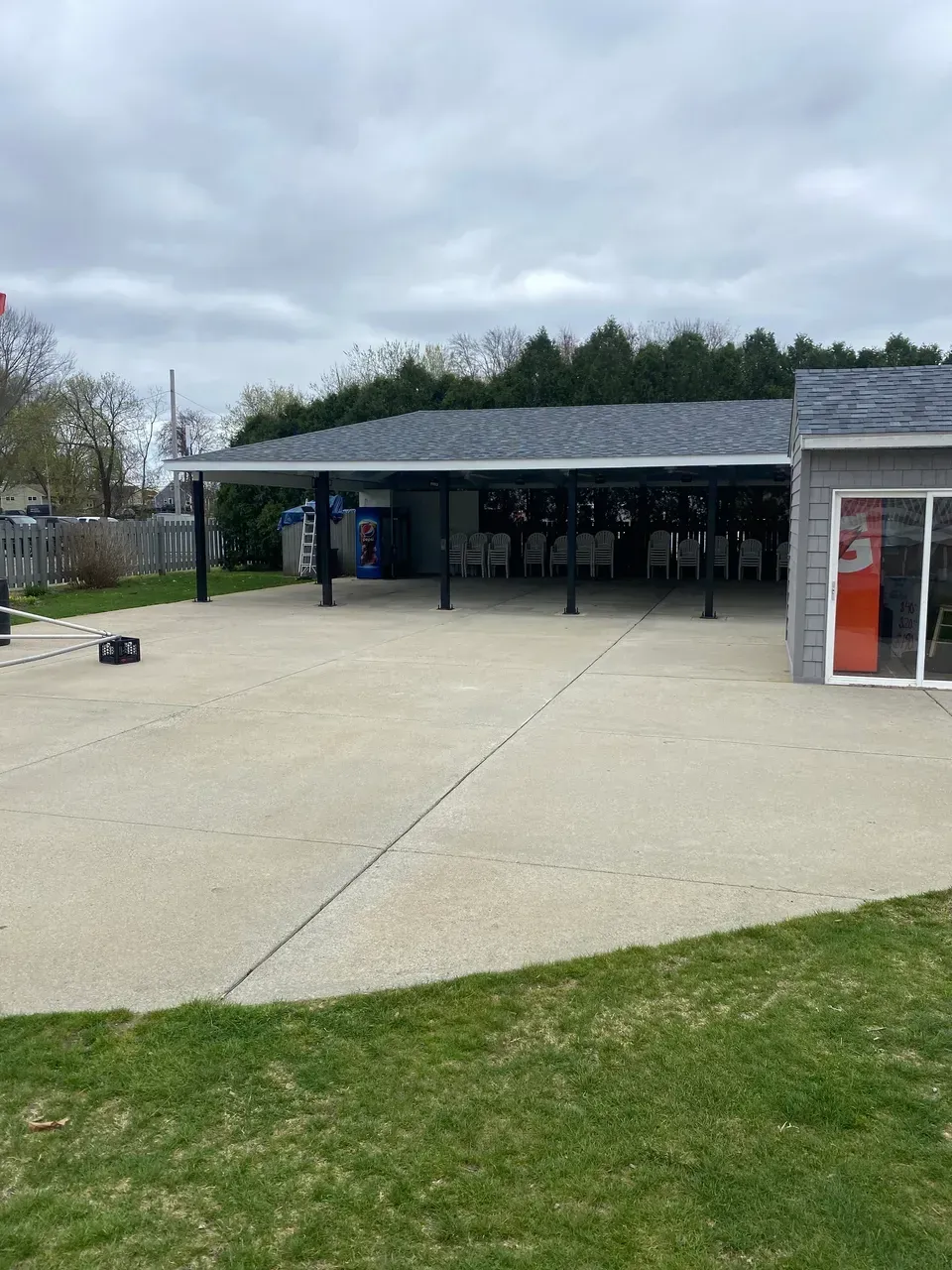 Outdoor pavilion with a gray roof, concrete courtyard, and grass under an overcast sky