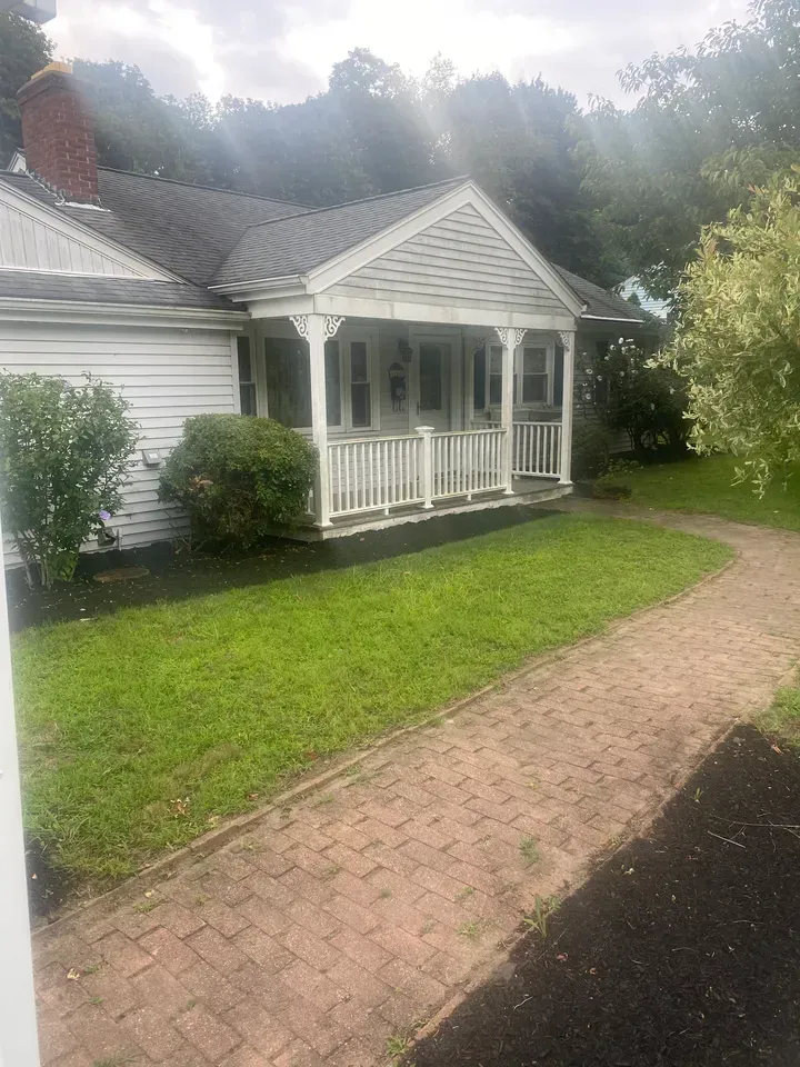 White house with a small front porch, green lawn, and brick walkway beside a driveway.