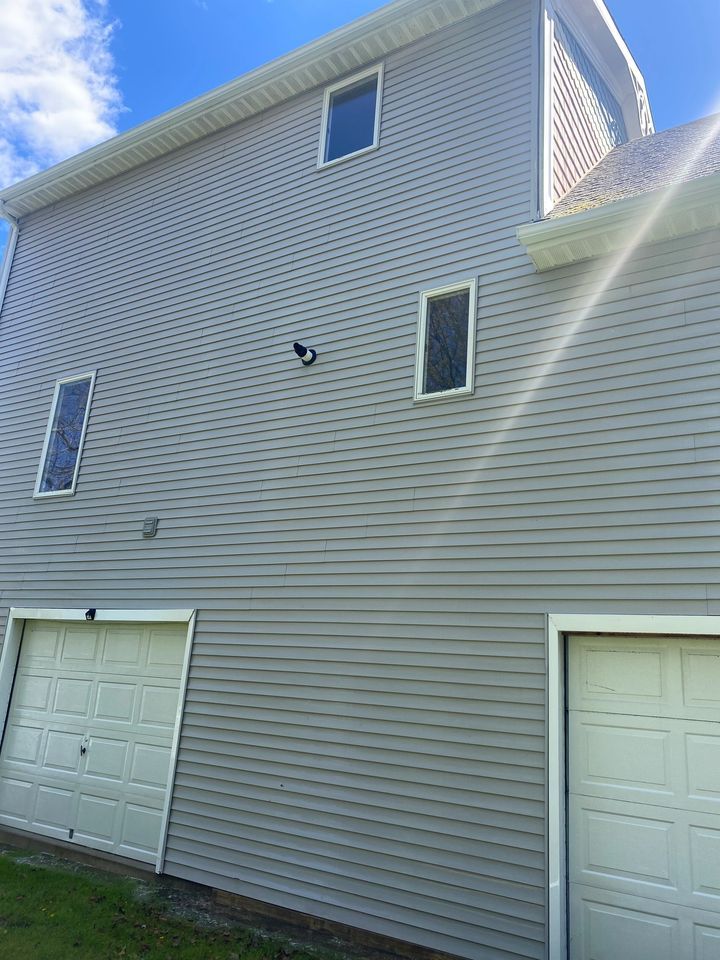 Exterior side of a gray house with two garage doors and several windows under bright sunlight