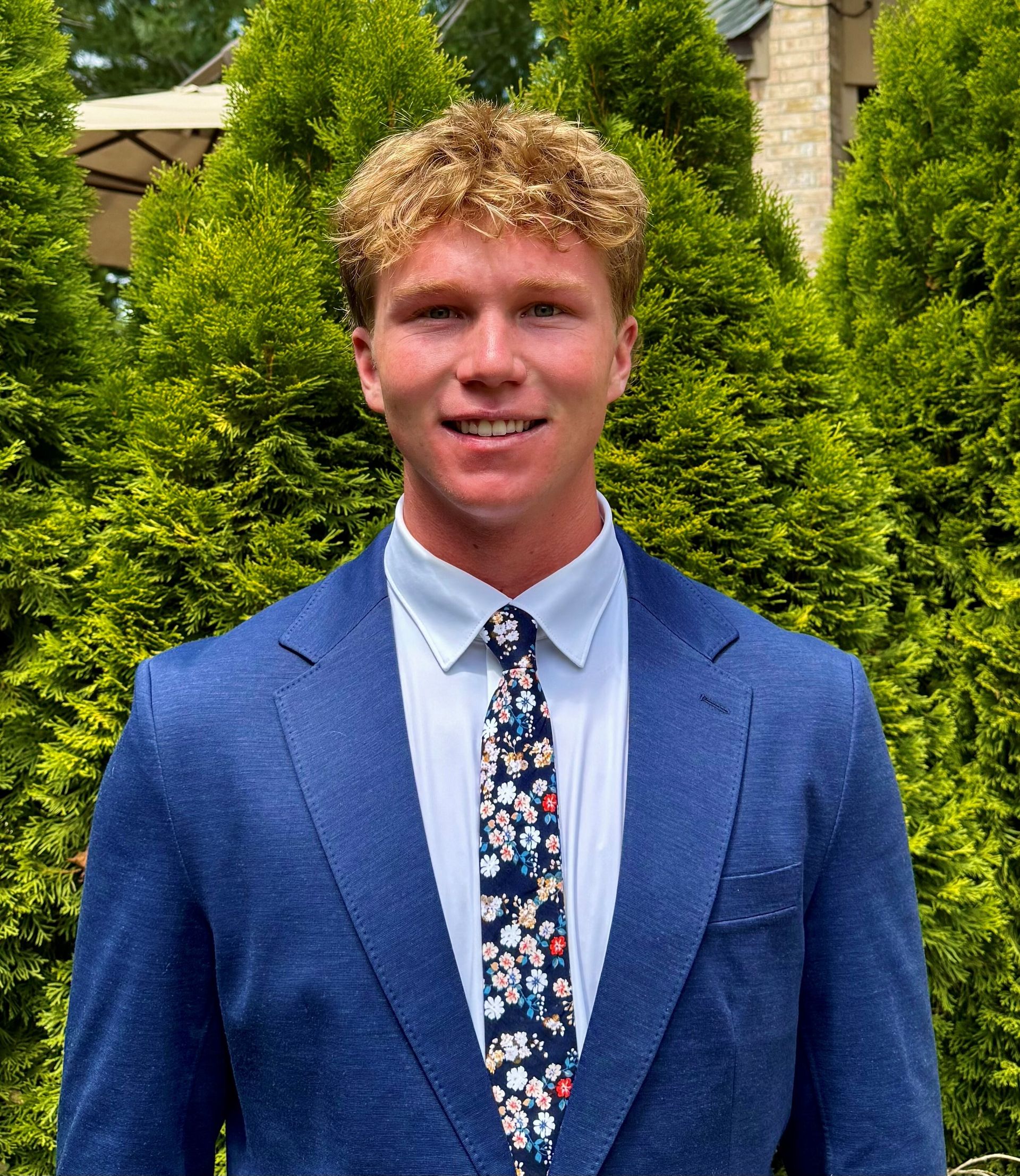 A woman with long black hair is standing in front of a wooden fence.