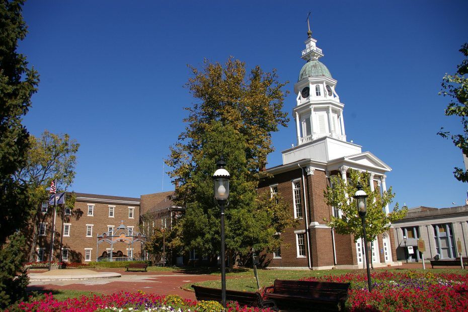 Brick courthouse with white tower and dome under a bright blue sky; benches and flowerbeds in the foreground.