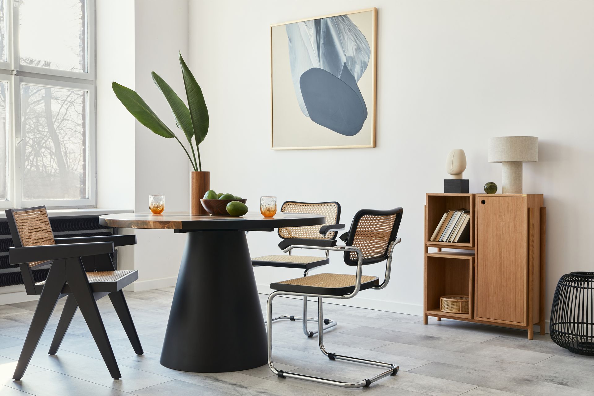Modern dining room with black round table, two lounge chairs, wooden cabinet, and abstract wall art
