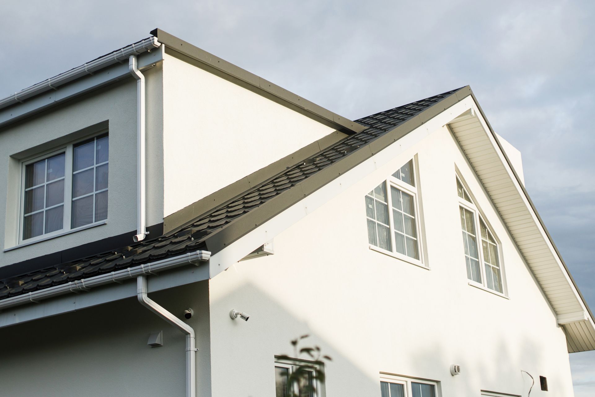 White house with dark roof, windows, and rain gutters, against a cloudy sky.