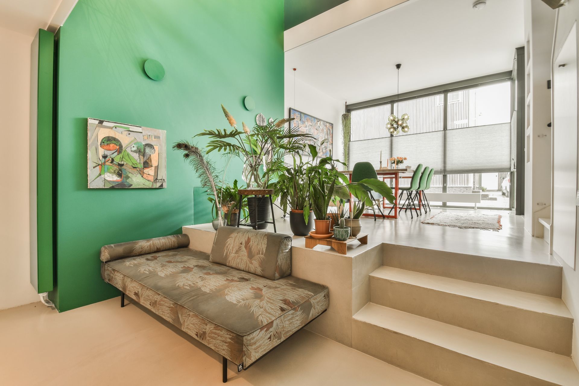 Interior with green accent wall, plants, sofa, and steps leading to dining area.