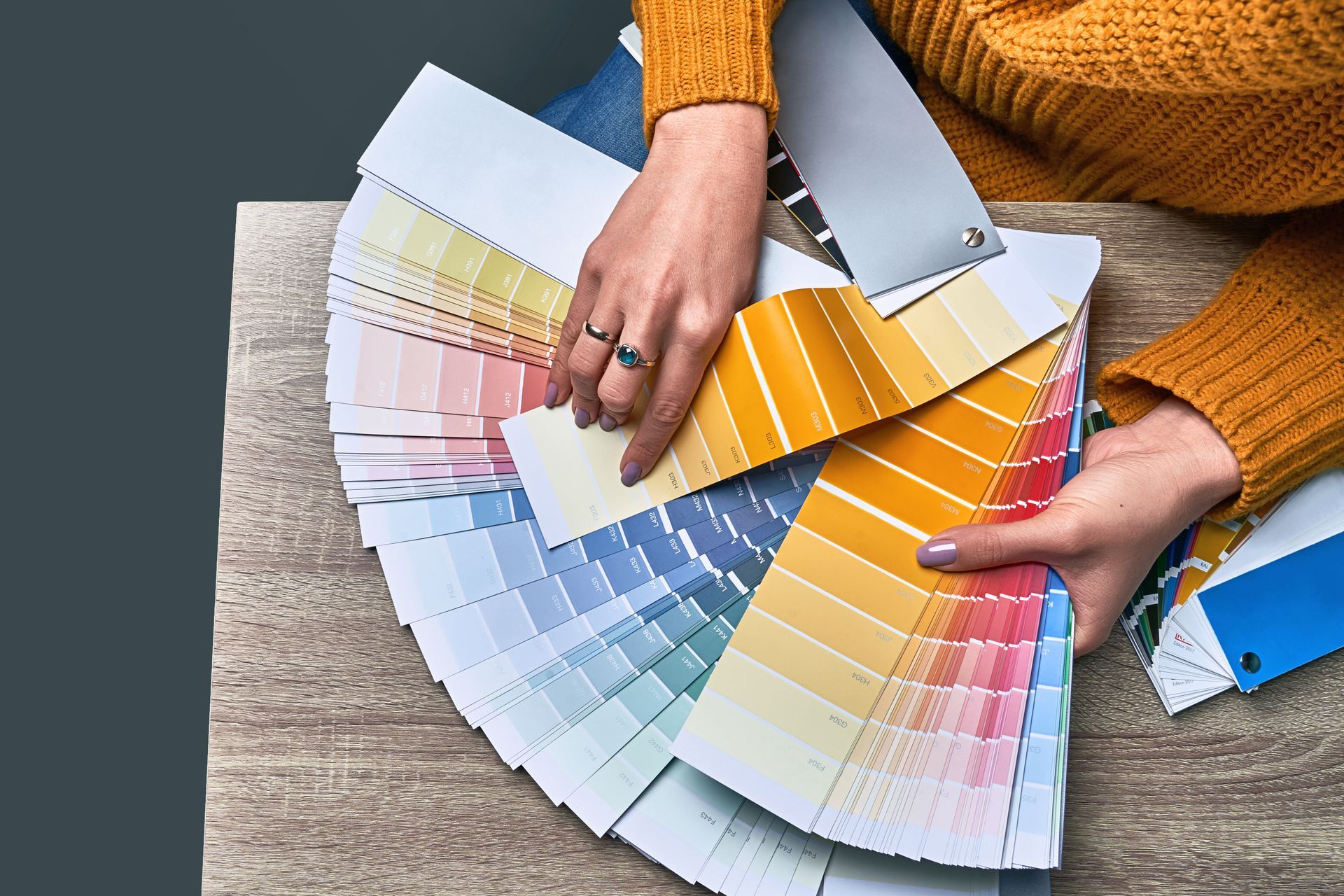 Hands fanning out paint color swatches on a table, with one selected in orange hues