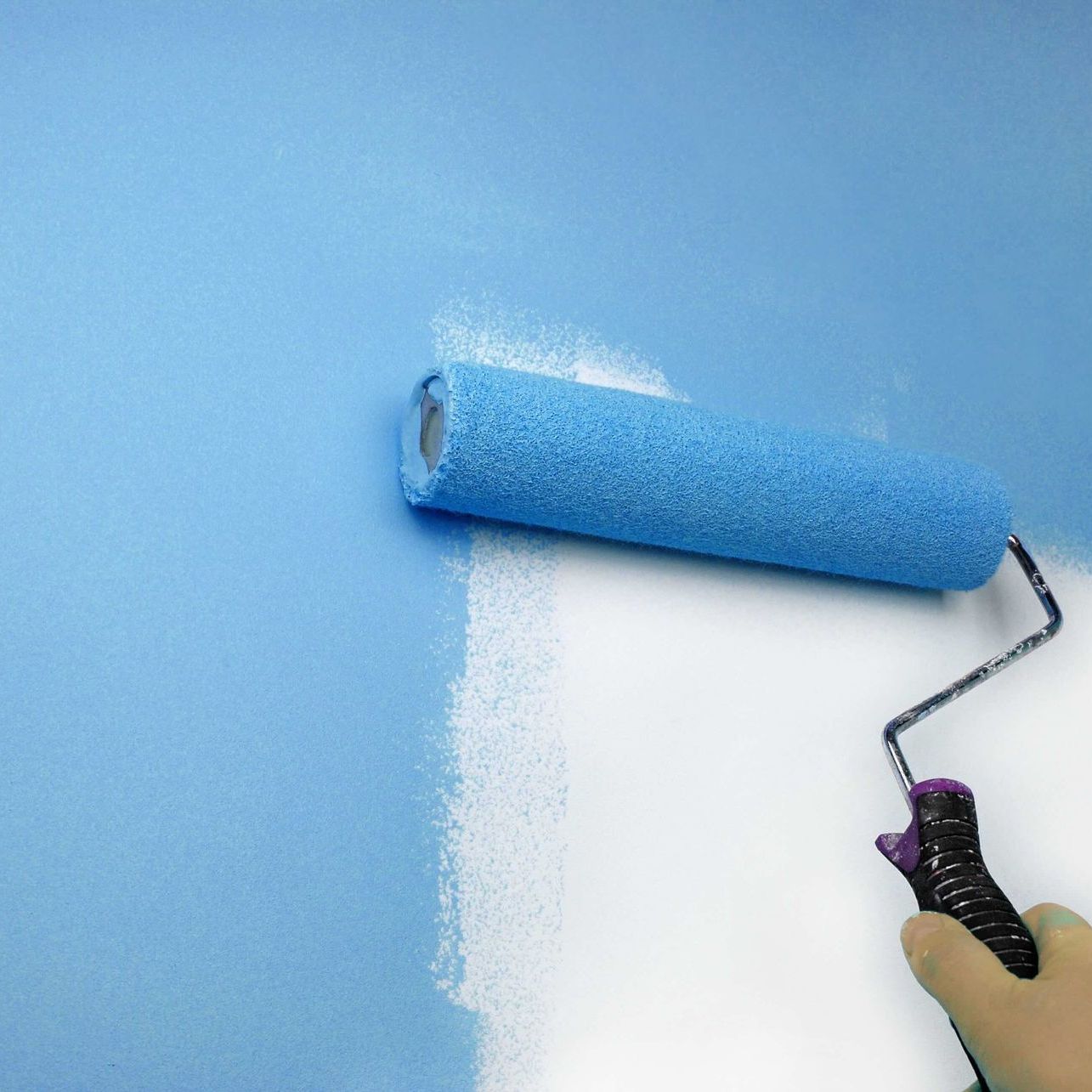 A person is painting a wall with a blue paint roller.