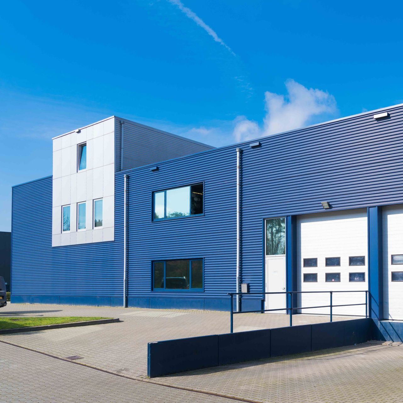 A large blue building with white garage doors and a ramp leading to it.