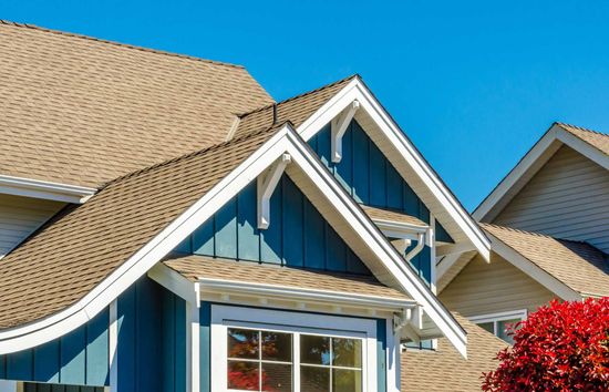 The roof of a house with a blue siding and a tan roof.