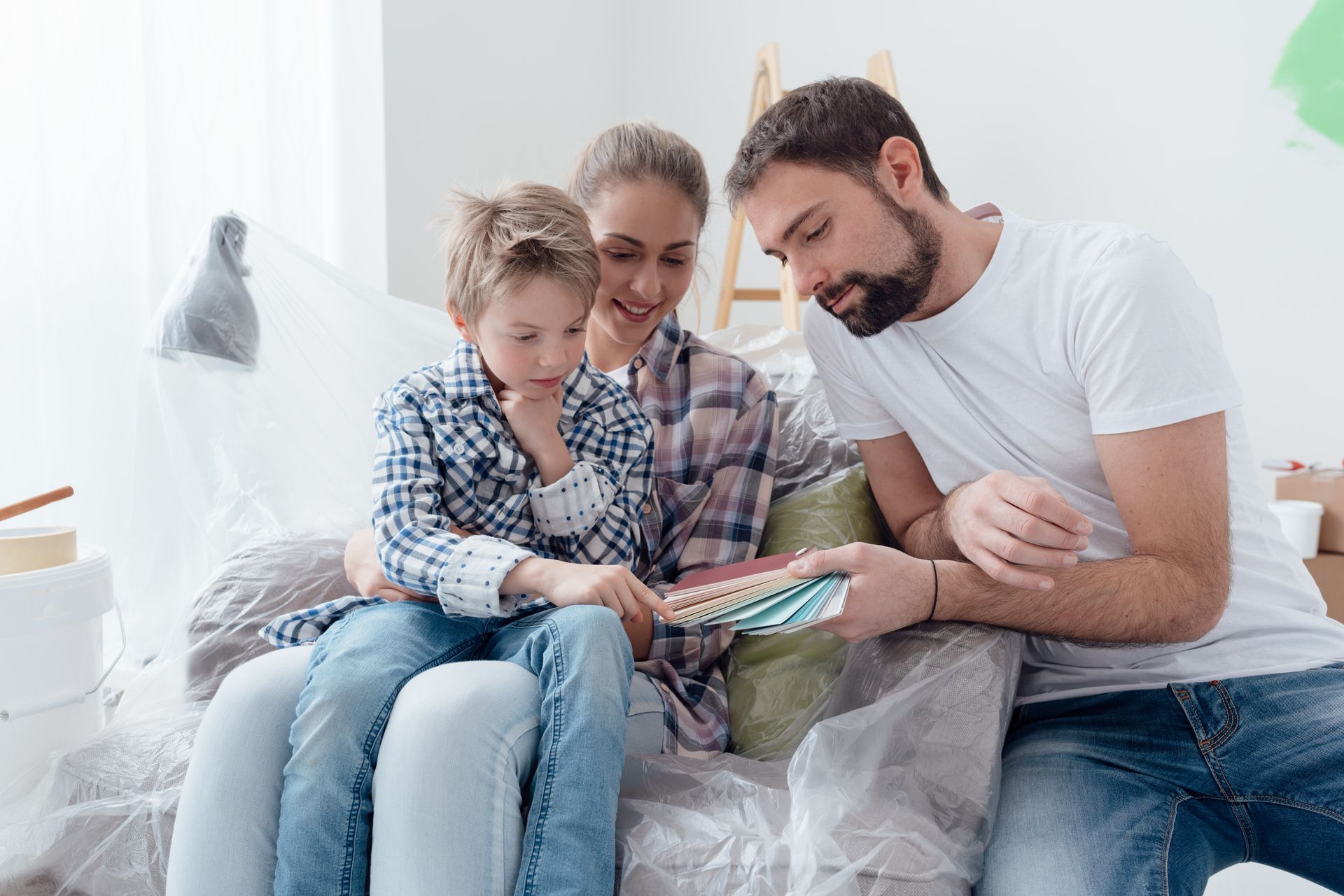 Family choosing paint swatches, with child sitting on mother's lap, in a room with paint supplies.
