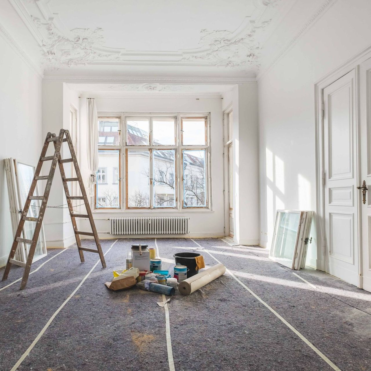 An empty room with a ladder and paint supplies on the floor.